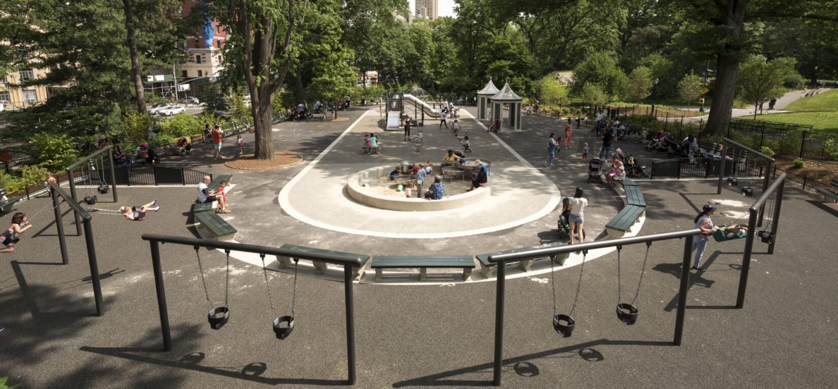 A wide-angle view down the length of the playground, shot from above and behind a row of infant swing sets.