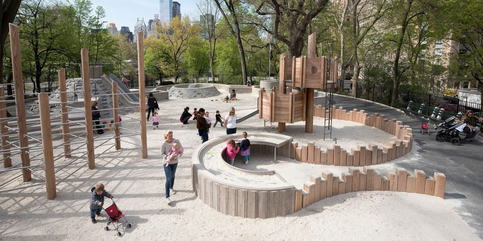 Children and caregivers playing at the sandy end of the playground, in Spring.