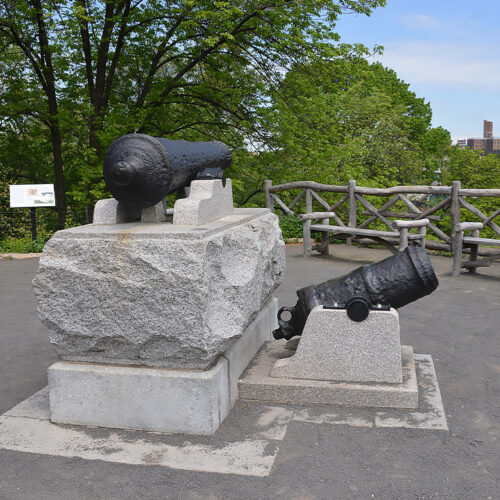 The cannon of Fort Clinton, surrounded by rustic seating and fences.