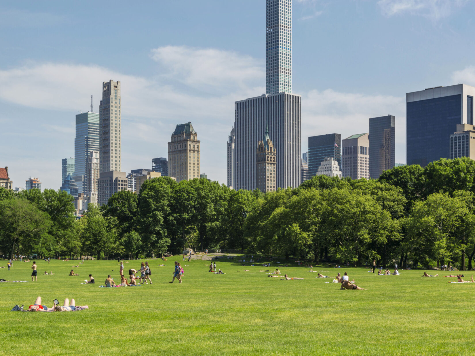 Parkgoers lounge on Sheep Meadow, with the skyscrapers of Manhattan's East Side filling the horizon.