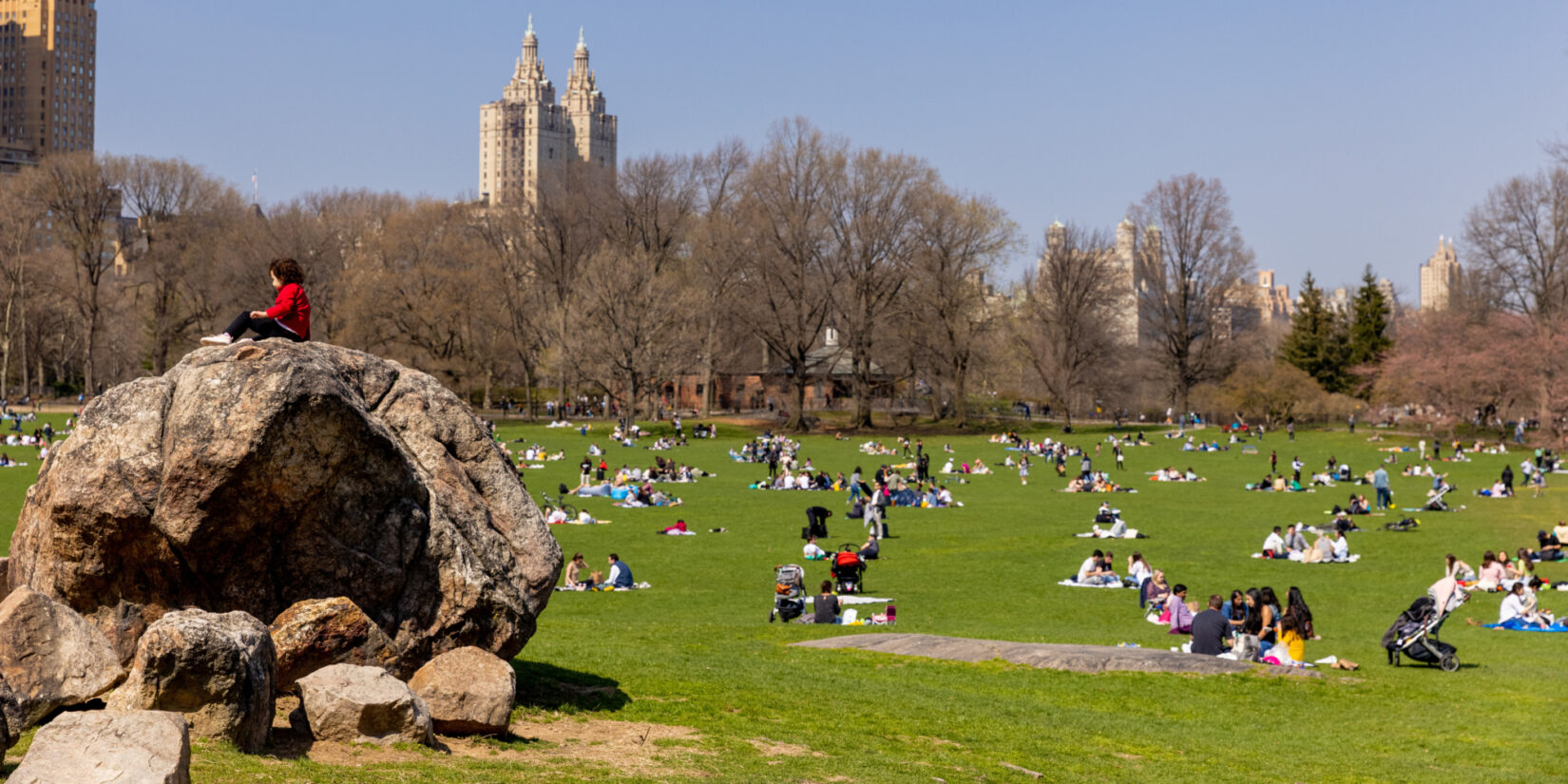 Park-goers on the Sheep Meadow enjoying a crisp Fall day. One visitor sits atop a large boulder.