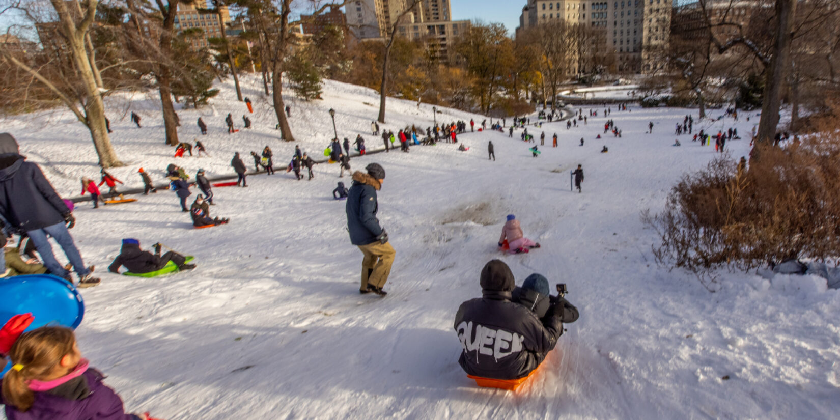 Kids of all ages enjoying sledding under a cold blue sky