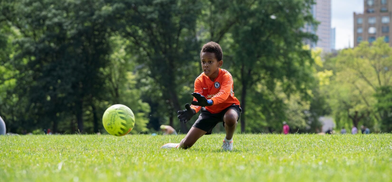 A young goalie keeps his eye on the ball on the North Meadow with the skyline in the background