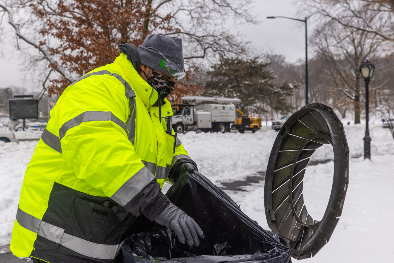 Staff member Raymond Acosta opens a trash can on a cold day in a snow-covered landscape.