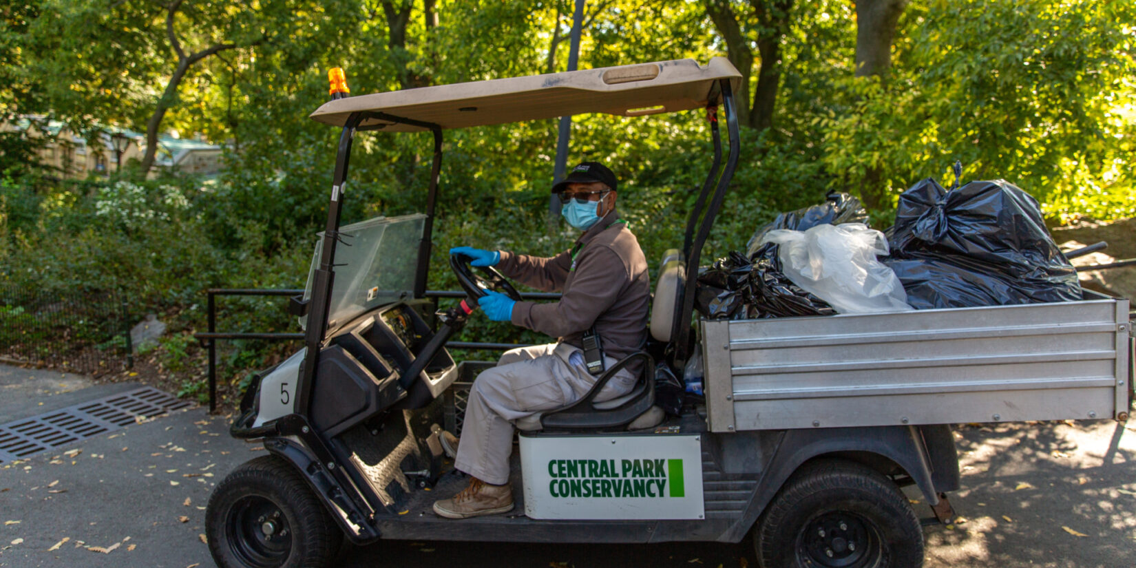 Staff member Rolly Tejada at the wheel of an electric cart used to haul small trash bags through Central Park.