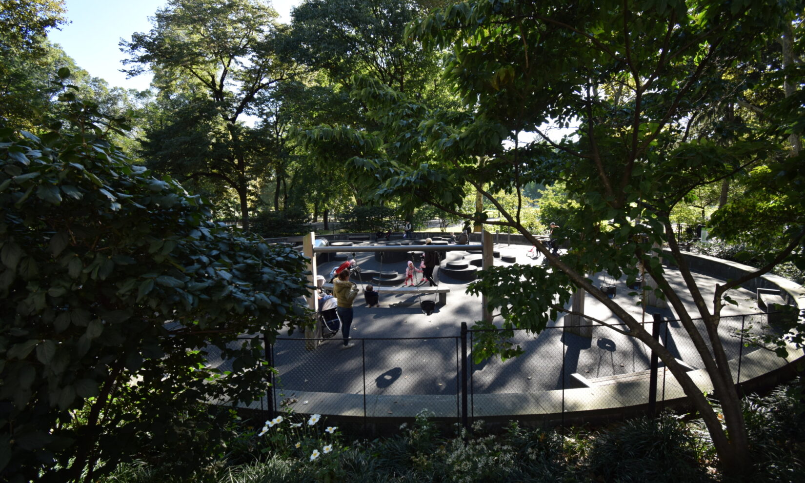 The playground is shown under a dappled, shadowy canopy of lush trees.