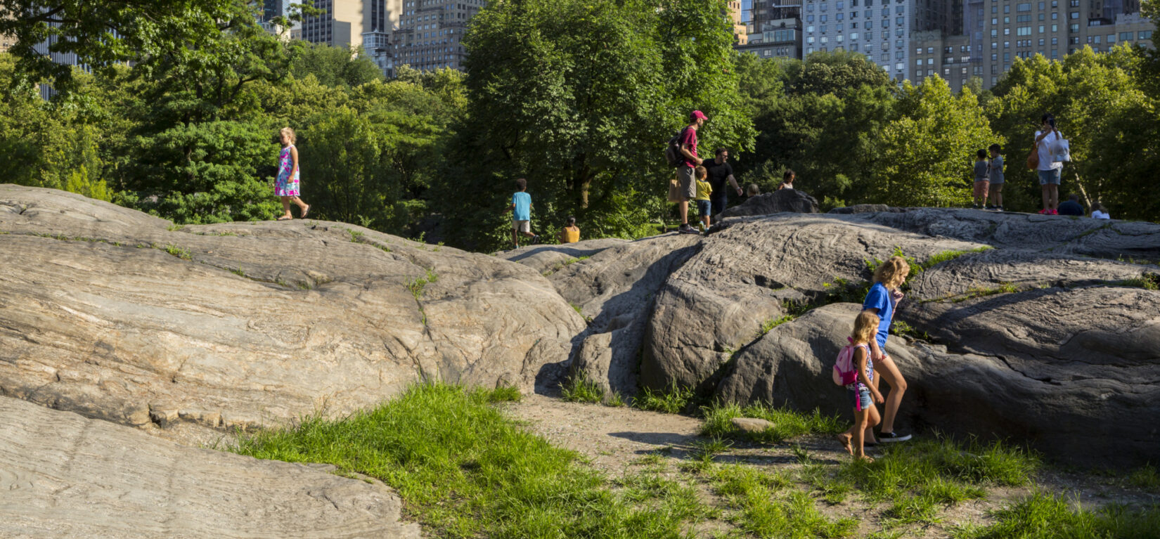 Children clamboring on Umpire Rock, on a summer day, with the skyline in the background