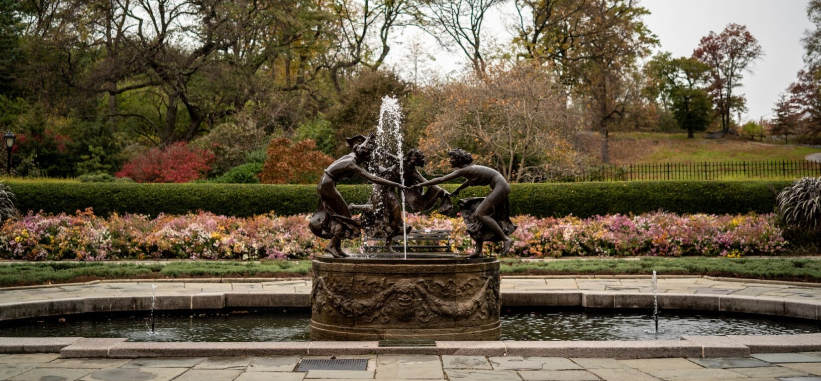 The fountain is pictured in fall with flowers and trees reflecting the season