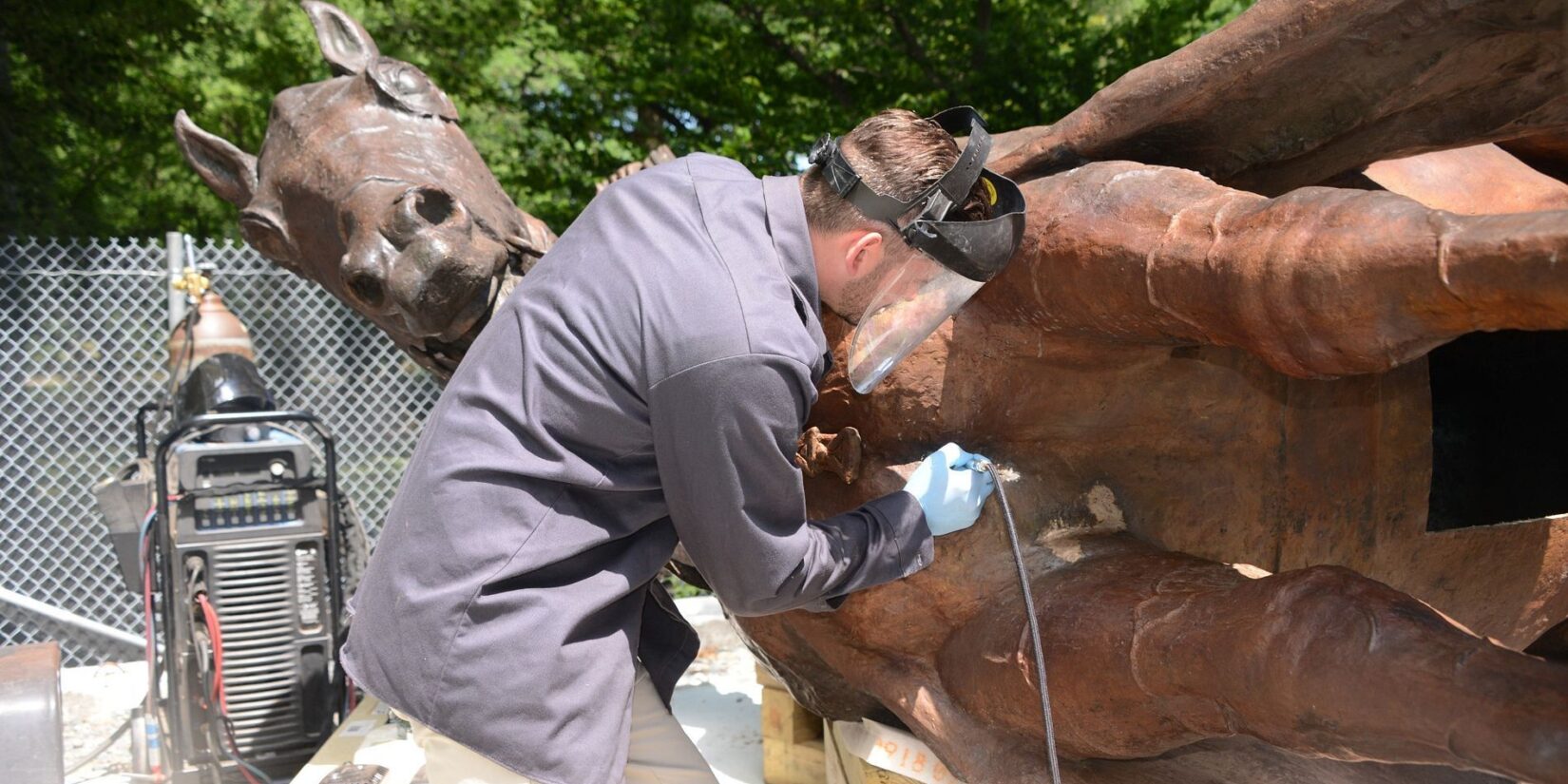 A welder works on the horse as the statue lays on one side.