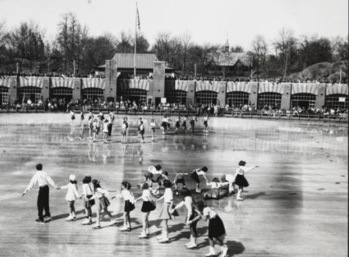 The rink is shot in black and white showing a brick pavilion and skaters in formation