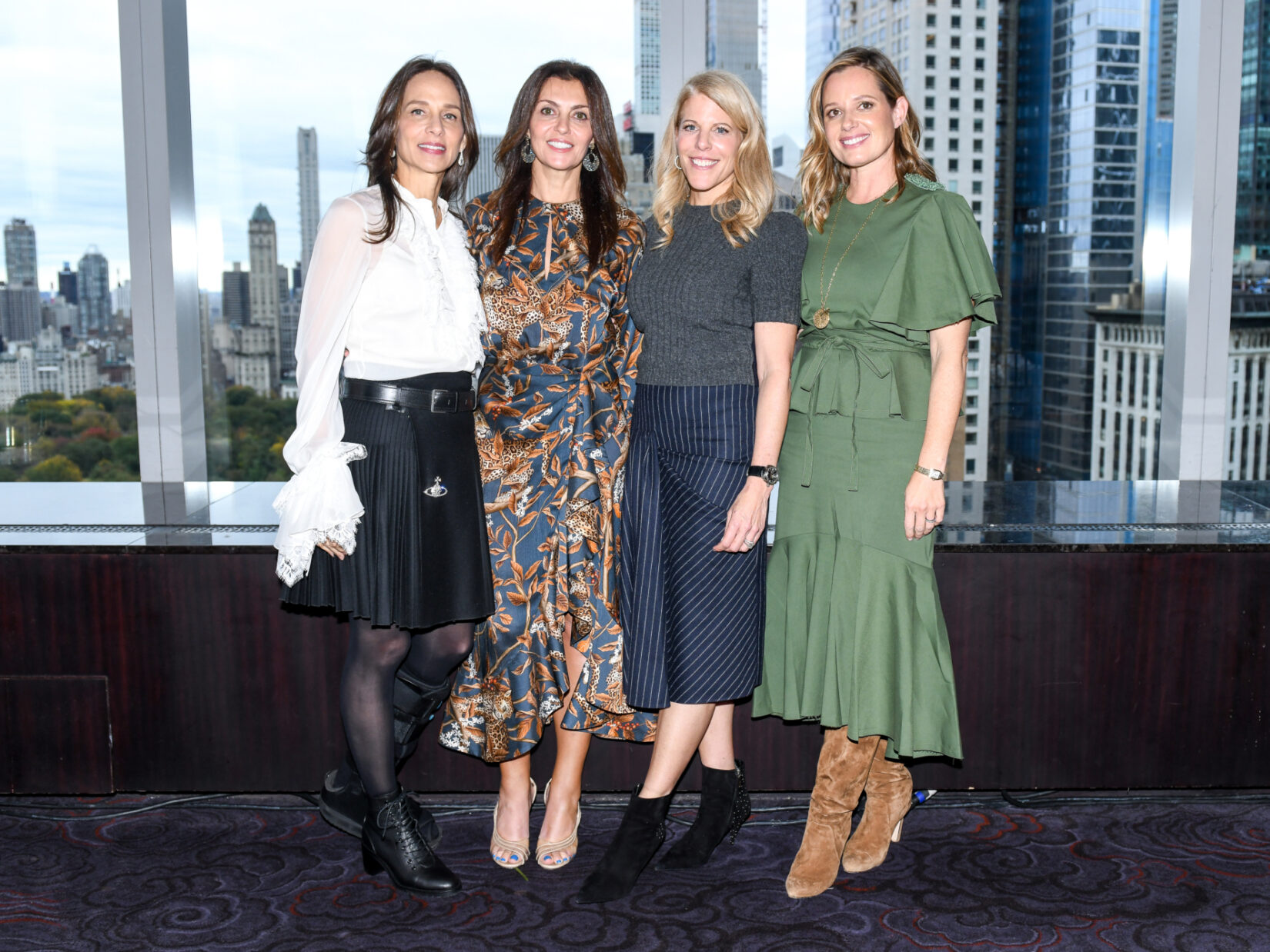 Members of the Women's Committee pose in front of a window with the NYC skyline behind them