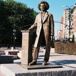 The Douglass statue faces into the sun with the skyline of Harlem behind him.