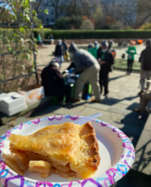 A delicious slice of apple pie on a paper plate, with Conservancy volunteers toiling in the background.